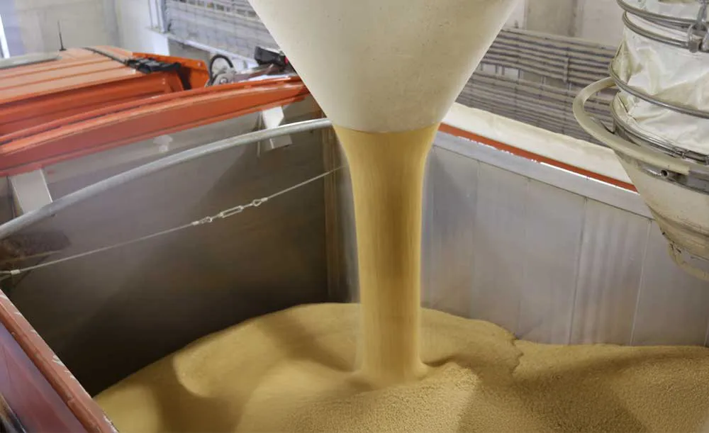 Compacte, stofvrije productstraal uit de Dust Reduction Hopper tijdens verlading, voor veilige en efficiënte verwerking van bulkproducten.